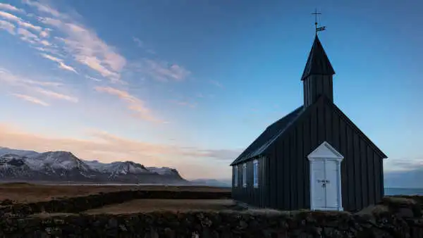 A black and white church in the foreground, mountains and ocean in the background